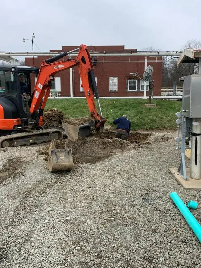 Two workers are operating a Perma-Liner installation machine surrounded by tools and hoses at a construction site.