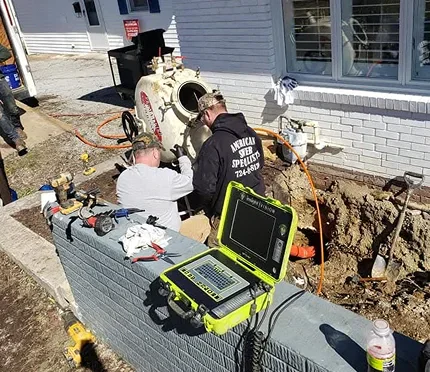 Two technicians work on a sewer inspection job near a trench, using equipment and a monitor to assess the situation.